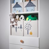 White shelf with decorative storage boxes featuring cat and tree designs, containing stuffed animal toys.