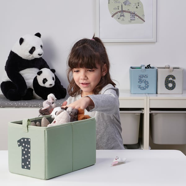 A young girl organizes toys in a labeled fabric storage box, learning to count while keeping her room tidy.