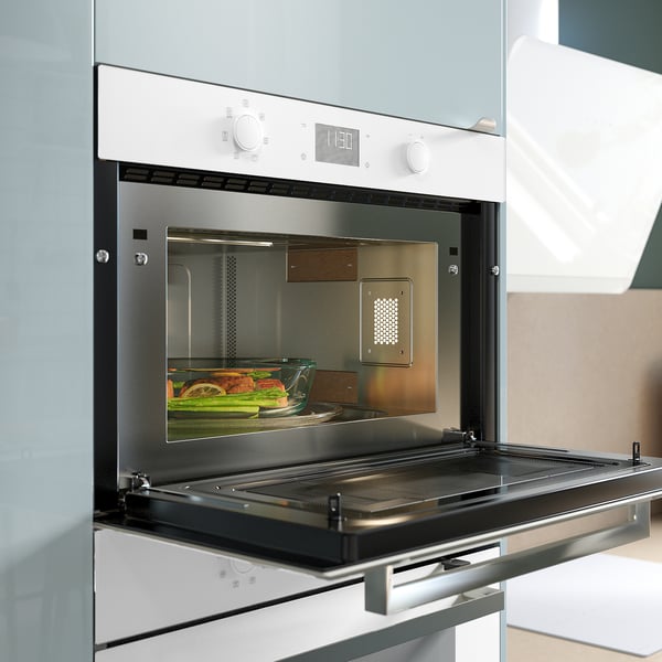 Modern built-in microwave in white with black door open, displaying veggies inside.