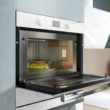 Modern built-in microwave in white with black door open, displaying veggies inside.