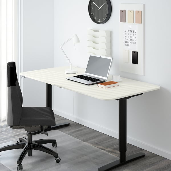 Modern home office with white BEKANT desk, gray chair, laptop, lamp, clock, and calendar.