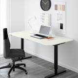 Modern home office with white BEKANT desk, gray chair, laptop, lamp, clock, and calendar.