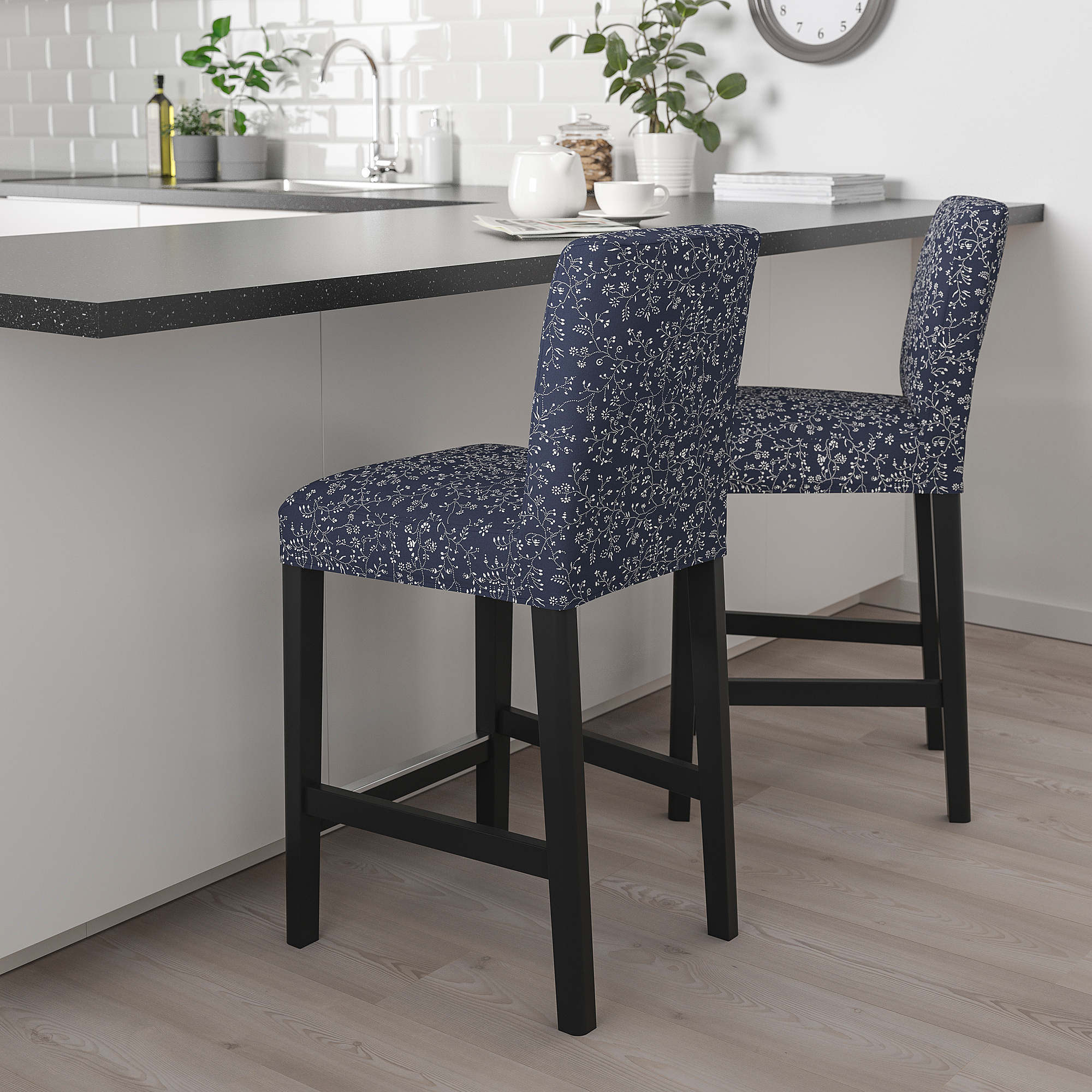 A pair of black and floral-patterned BERGMUND bar stools sit against a gray kitchen island, contrasting the white background and adding a cozy touch.