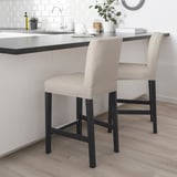 Modern beige bar stools with black legs, cushioned seats & backs, fitting under a counter in a kitchen.