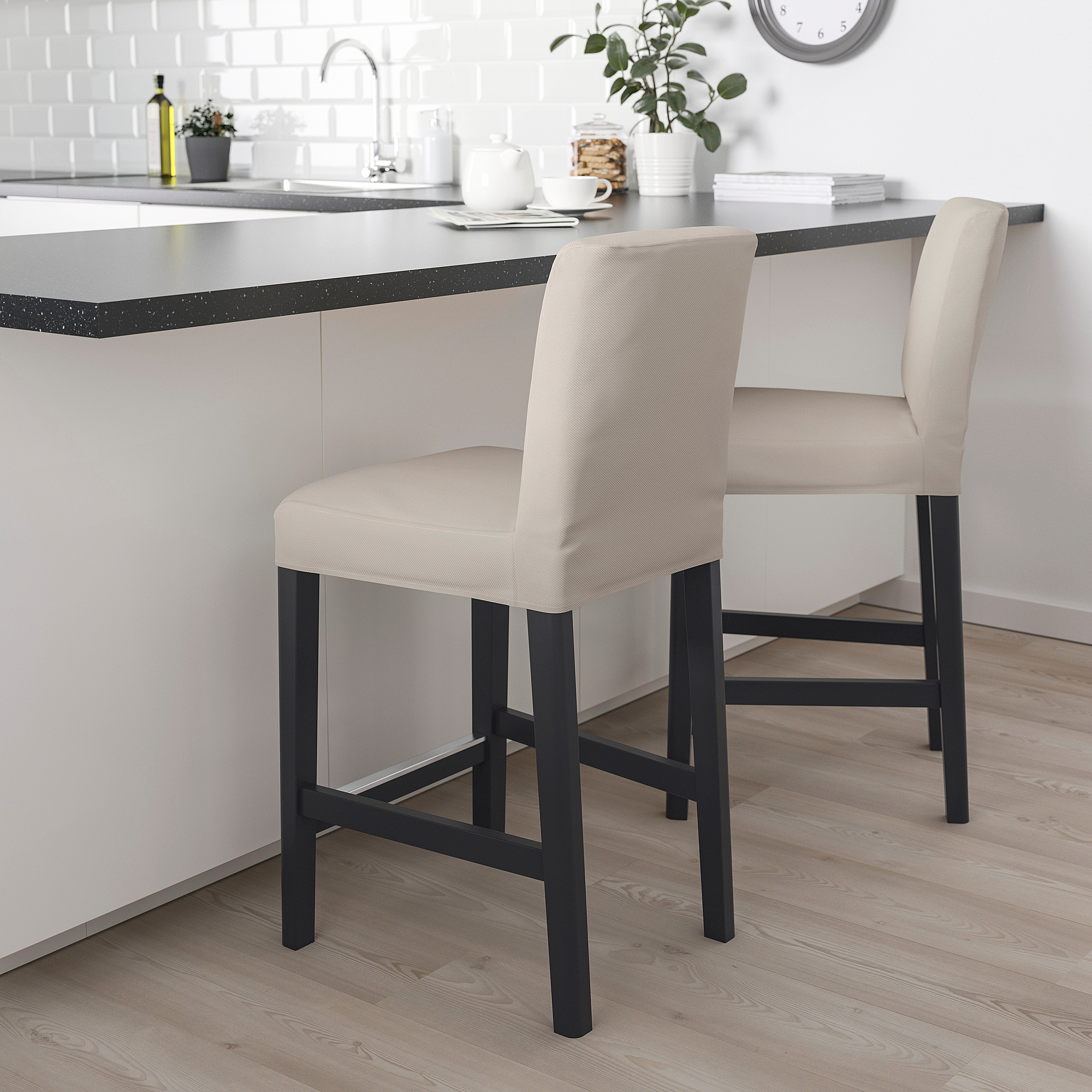 Modern beige bar stools with black legs, cushioned seats & backs, fitting under a counter in a kitchen.