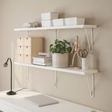 Wall-mounted shelf with brackets holding containers, plant, and wooden figure, with a lamp and laptop on desk below.