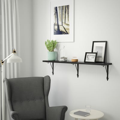 A cozy living area with a BERGSHULT black shelf holding a plant, decor, and a frame. Below, a table holds a book and a glass.