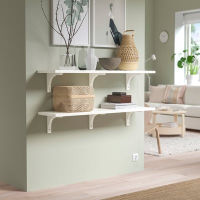 White BERGSHULT wall shelves with woven baskets, vases, and framed art. Bright, minimalist living room with light wood floor.