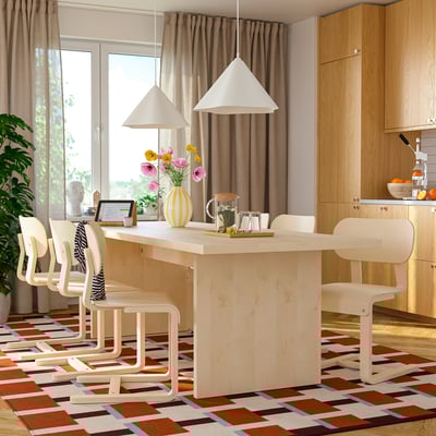 Modern dining room with large light wood table, six chairs, rug, and hanging lamps.