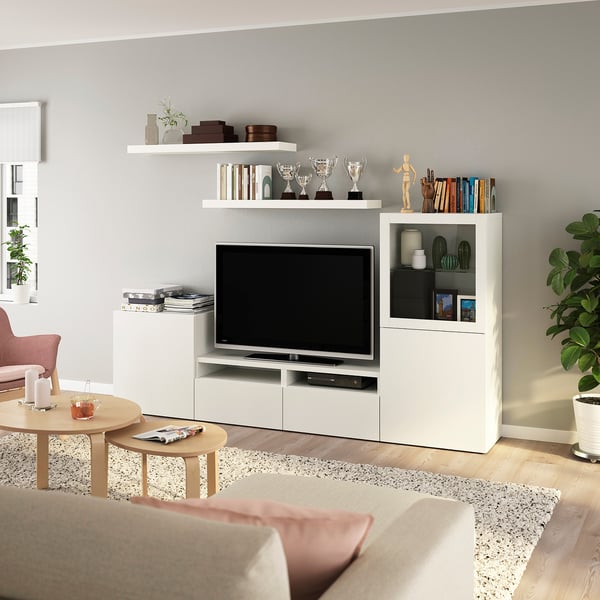 Modern living room with BESTÅ tv unit, flat screen, trophies, books, coffee table with candles, and a large beige chair.