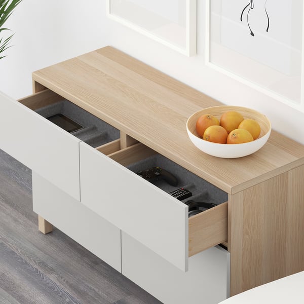 Light wooden sideboard with open drawers showing remote and game controller. White bowl with oranges sits atop.