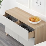 Light wooden sideboard with open drawers showing remote and game controller. White bowl with oranges sits atop.
