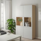 Modern living room with tall white BESTÅ shelf unit. Displaying vases, books, and plants. Size: tall, fits beside window and couch.