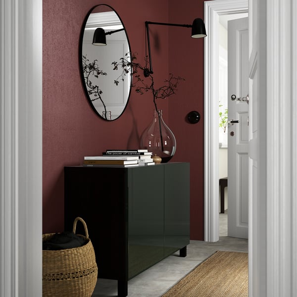 Dark green BESTÅ sideboard with mirror, lights, dried plant, books, and vase. Character count: 63