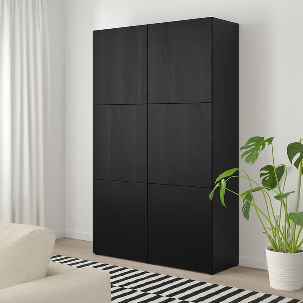 Black BESTÅ 6-door unit beside window, next to beige sofa and striped rug, with green plant.