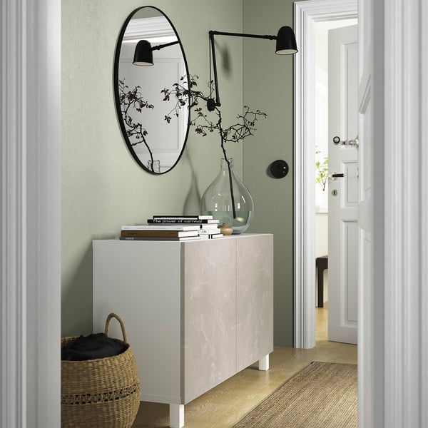 White marble BESTÅ sideboard against green wall with books, vase, mirror & lamp.