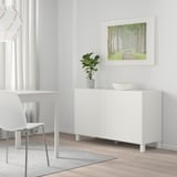 Modern minimalist room with BESTÅ sideboard, plant, chair, and table. Brightly lit with balance.