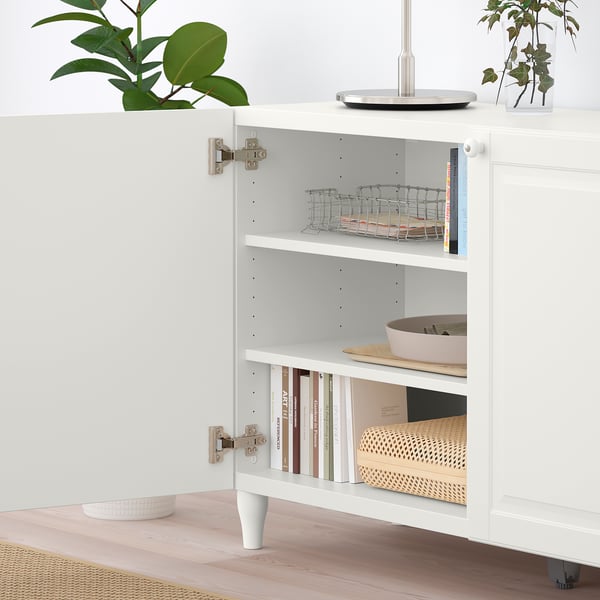 White cabinet with adjustable shelves holding items, including books and a basket, with open doors showcasing storage.