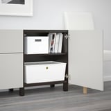 Open BESTÅ sideboard with adjustable shelves storing boxes and books. Legs elevate it from the floor.