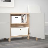 White BESTÅ sideboard, adjustable shelves, two drawers, one open with items, raised legs.