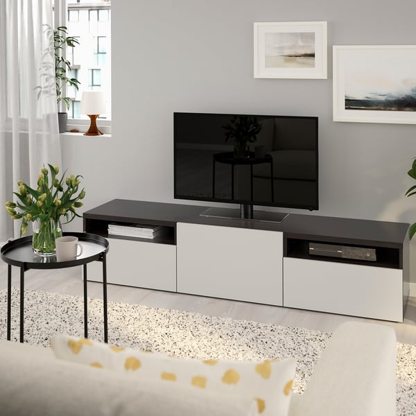 Modern living room with BESTÅ tv bench in black and white. Flat screen tv on top, drawer storage, yellow flowers, lamp, and nature artwork.