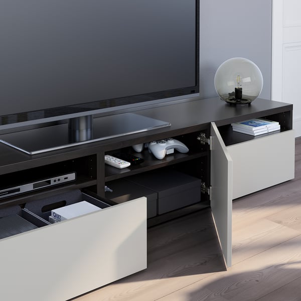 Modern tv stand with open drawers, showing game controllers and remotes. A large flat-screen tv sits atop.