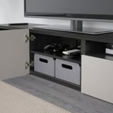 Tv stand with open shelf holding gaming controls and remotes, featuring cable management and wall-mount capability.