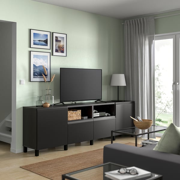 Modern living room with BESTÅ tv bench in black. Flat screen tv, grey curtains, wooden floor, and green walls with art frames.