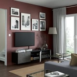 Modern living room with maroon walls, BESTÅ tv bench, glass coffee table, large window.