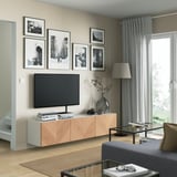Modern living room with BESTÅ tv bench, flat-screen tv, photos, adjustable shelves, vase, glass table, grey sofa, large windows.