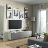 Modern living room with BESTÅ tv bench in gray, flat screen tv, framed photos, wooden floor, and a gray curtain.