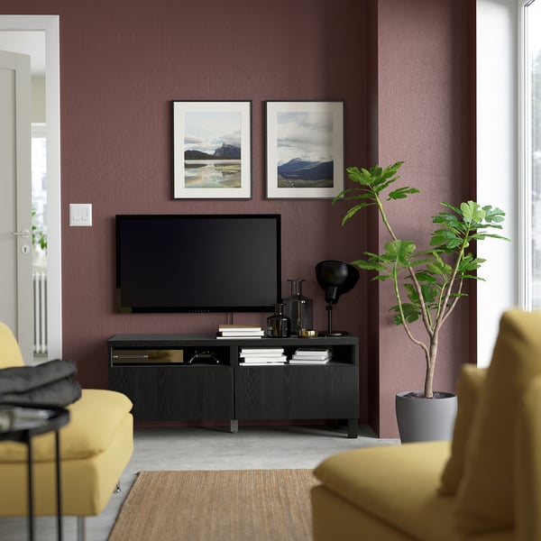 Modern living room with dark walls, black tv unit, art, tv, decor, yellow sofas, and large green plant.