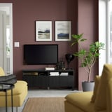 Modern living room with dark walls, black tv unit, art, tv, decor, yellow sofas, and large green plant.