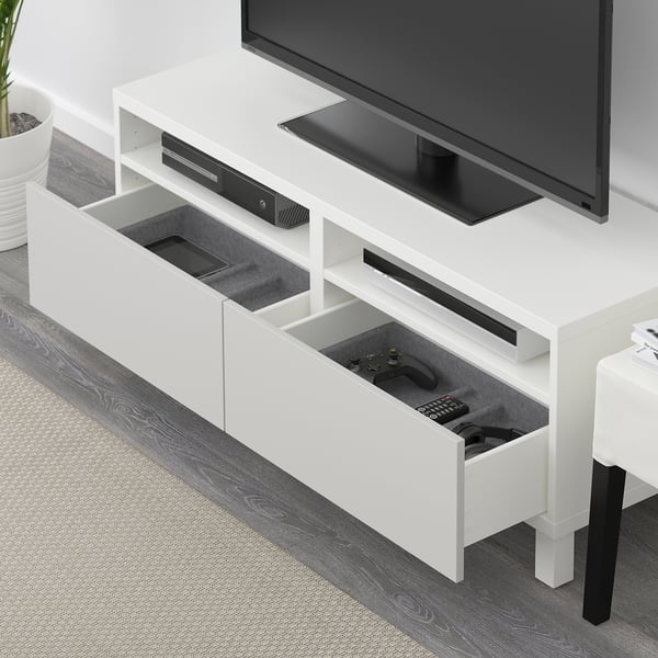 White BESTÅ tv stand with drawers open, showing remote and gaming controller storage, led cable management, and black flat-screen tv placed on top.