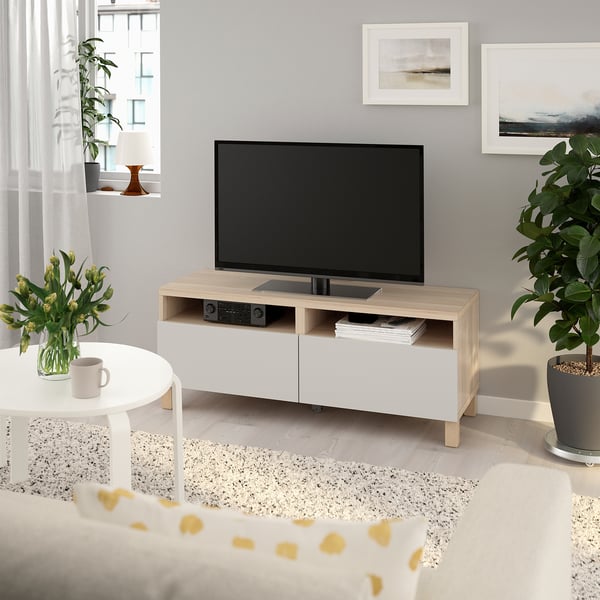 Modern living room with BESTÅ tv bench, books, device, coffee table, mug, flowers, and wall frames.
