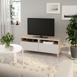 Modern living room with BESTÅ tv bench, books, device, coffee table, mug, flowers, and wall frames.
