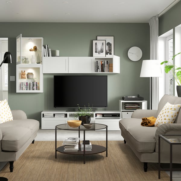 Modern living room with BESTÅ unit, clock, table, books, plants.