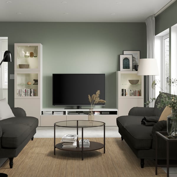 Modern living room with mounted tv, grey sofas, glass coffee table, floor lamp, and BESTÅ storage.
