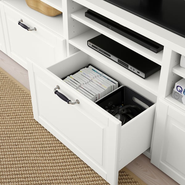 White BESTÅ tv stand with open drawer showing game controllers and dvds. Tv and soundbar placed on top.