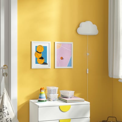 Yellow wall with white art, basketballs, pastel shapes. White dresser, toys, books, cloud lamp.