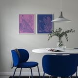 Pink & blue BILD posters above table with blue chairs, minimalist shapes, vase with greenery.