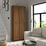 Wooden BILLY bookcase next to stairs & cozy chair, tall with double doors.