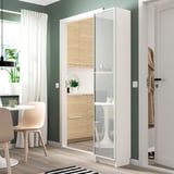 Modern BILLY bookcase near kitchen. Tall, glass-fronted, beside chair, wooden cabinets, potted plant.