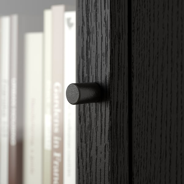 Close-up of modern, black cylindrical handle on dark wooden drawer; sleek and stylish.