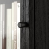 Close-up of modern, black cylindrical handle on dark wooden drawer; sleek and stylish.