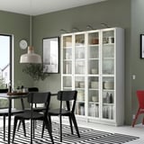 Modern dining room with BILLY white glass-door bookcases, black chairs, green walls, striped rug, and pendant light.