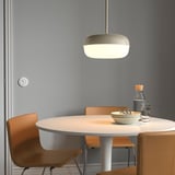 Modern dining setup with round table, 4 chairs, warm lamp, bowls, glasses, and cutlery by gray wall.