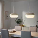 Two BLÅSVERK pendant lamps in beige hang above a dining table, emitting a soft light in a modern dining room setting.
