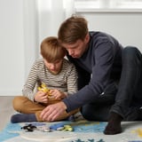 A child and man play with soft sea creature toys on a blue/yellow rug, promoting bonding and learning.