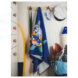 A colorful turtle-patterned blue bath towel hangs on a wooden hook next to a white wall and drawers with wooden knobs.